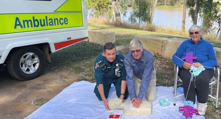 Two people with a CPR mannikin and a third with knitting