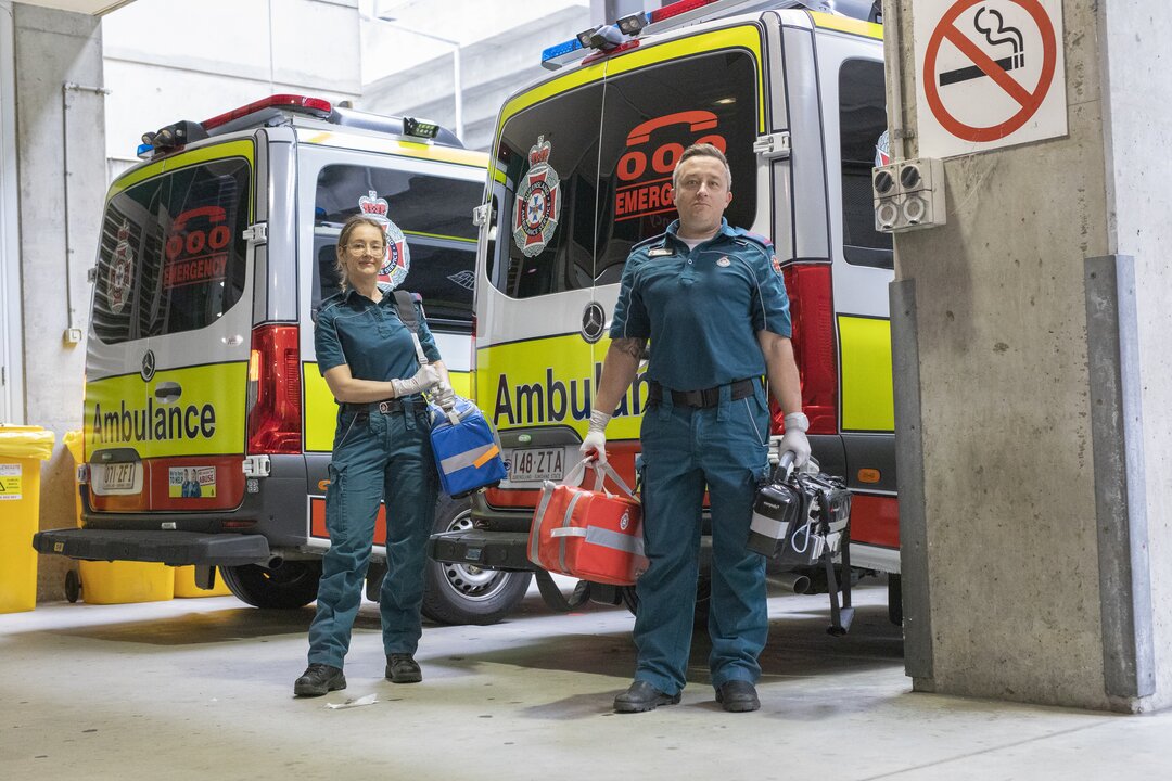 Photo of two paramedics holding their kit bags behind an ambulance