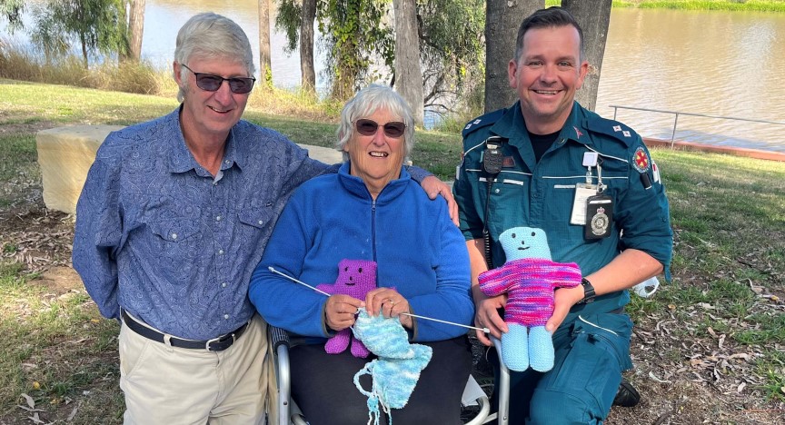 An elderly couple sit with a paramedic holding knitted teddies